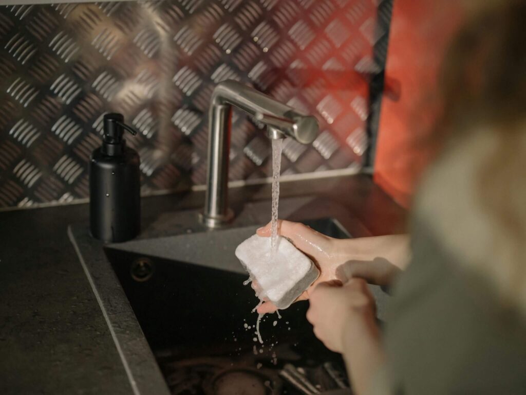Person washing a dish under running water in a kitchen sink.